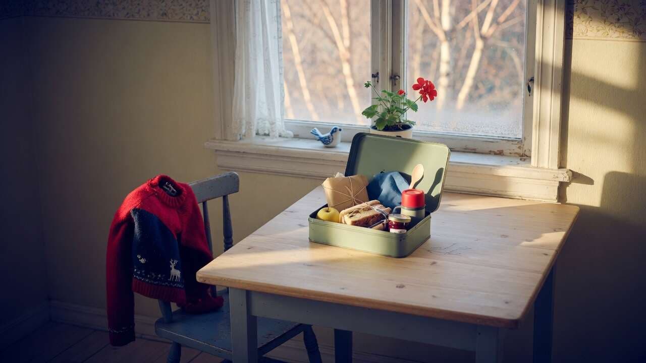En barnstol vid ett köksfönster med en öppen matlåda på bordet
